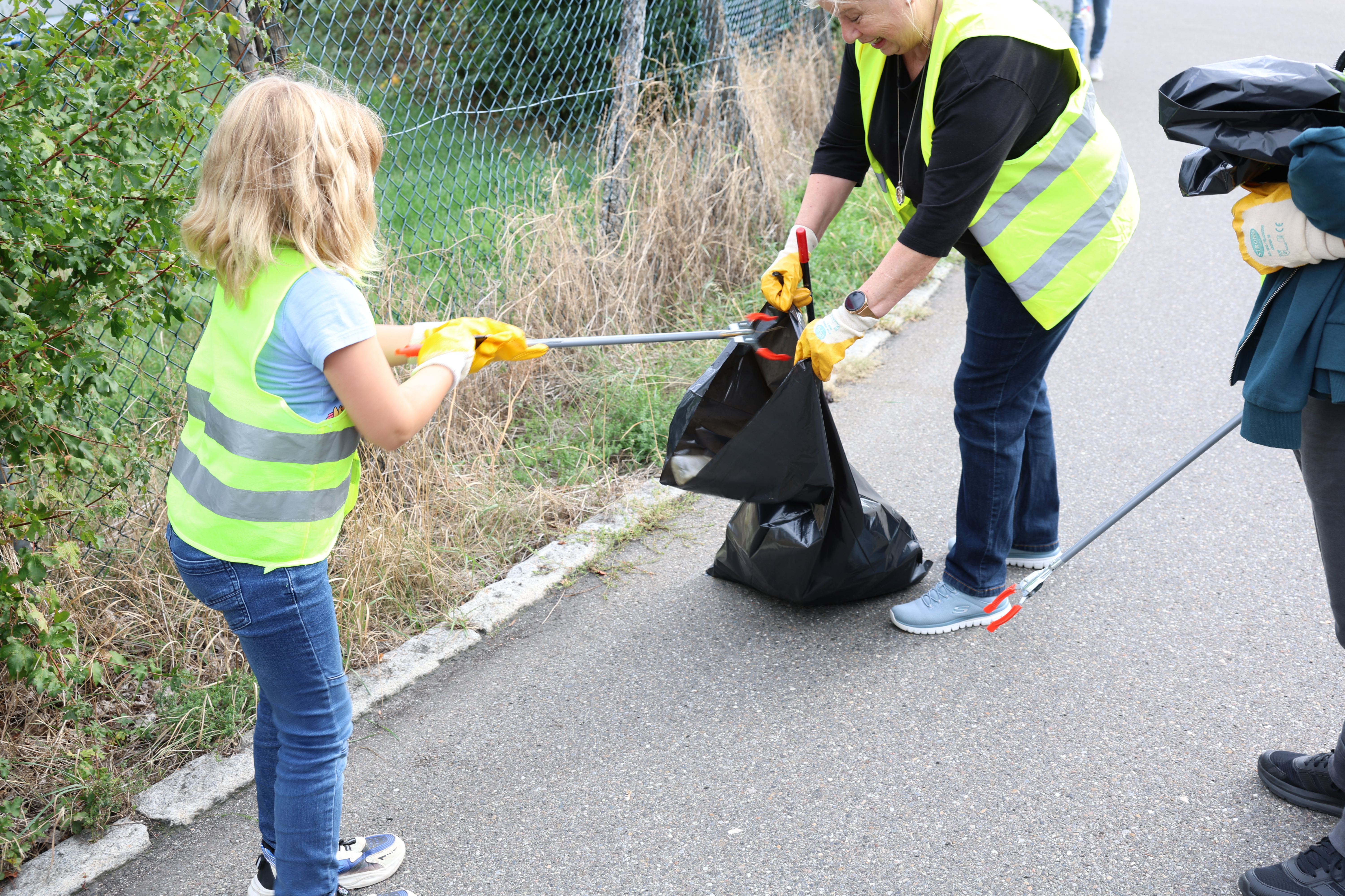 Ein Kind und eine Mitarbeiterin von dataTec sammeln beim World Cleanup Day 2026 gemeinsam Abfall ein und geben ihn in einen Müllsack.